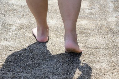 Çıplak ayaklı bir adam kirli beton zeminde yürüyor.