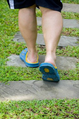 Kare çimentoyla yeşil çimlerde yürüyen bir adam.