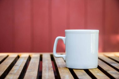 Beyaz kahve fincanı kırmızı arka planlı ahşap masada.