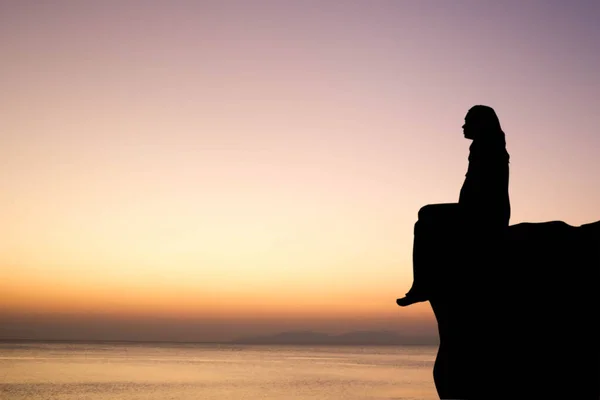 夕焼け空の崖の上の孤独な女のシルエット — ストック写真