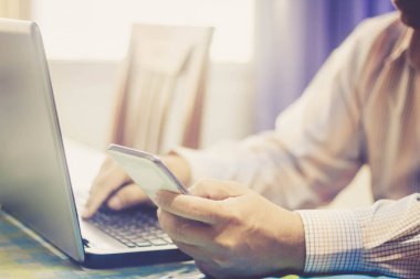 İşadamı dizüstü bilgisayarda çalışıyor ve klasik filtrede akıllı telefon kullanıyor.