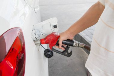 Adam benzin istasyonunda beyaz arabasına yakıt ikmali yapıyor.