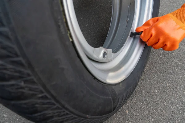 一只橙色手套袖子的特写镜头从汽车车轮上的乳头盖上扭下来 — 图库照片