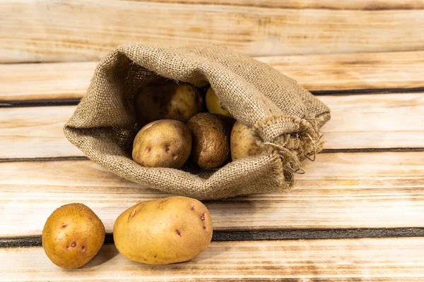 Fresh potatoes in an old bag on a wooden background. Free space for text.