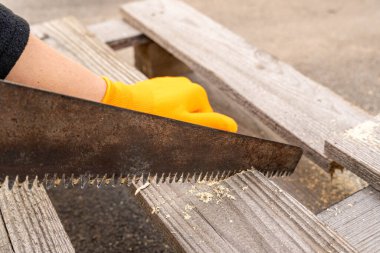Turuncu eldivenli bir el paslı bir testereyle tahtayı kesiyor. İnşaat ve yenileme konsepti