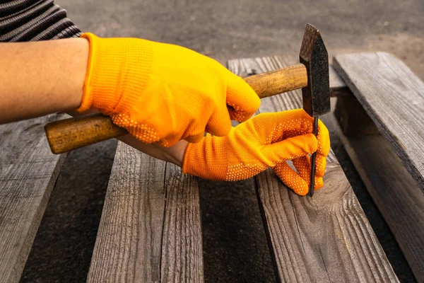 Hands in orange gloves hold a hammer and hammer a nail into the board