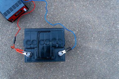 Tamirci aküyü şarj cihazına bağlar, arabanın aküsünü kontrol eder ve tamir eder.