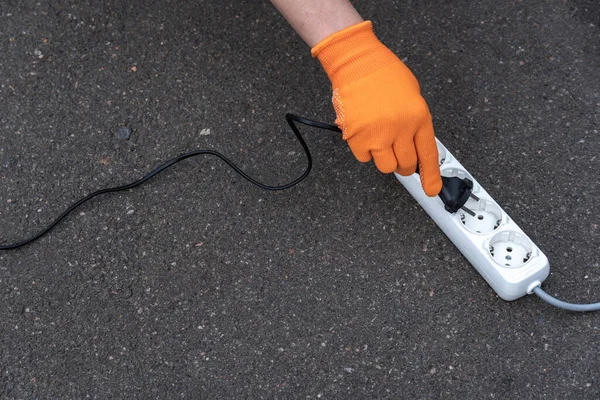 A hand in an orange glove inserts a power cord into a white extension cord on a gray background. Free space for text