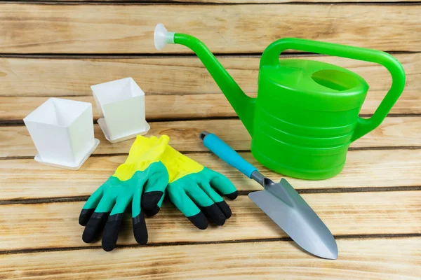 Shovel, gloves, hand sprinkler, flower pots on a wooden background. garden tools