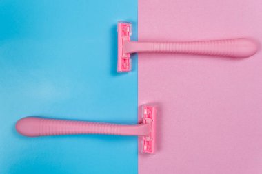 Fotokopi alanı olan mavi-pembe bir arka planda iki adet tek kullanımlık pembe tıraş bıçağı var..