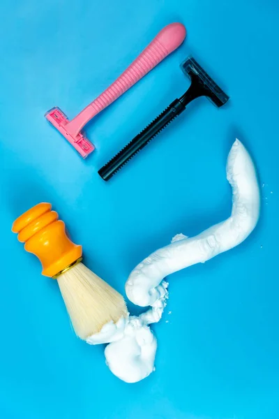 Gender inequality and stereotypes. The division of the sexes into men and women. Image of pink, black razors and shaving brush with foam on blue background