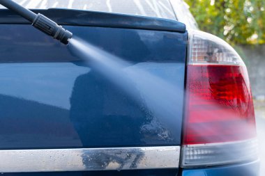 Basınçlı yıkama makinesiyle koyu renk bir arabayı yıkamak. Yüksek basınçlı yıkama hortumu arabanın arka farlarındaki köpüğü yıkar. Temizlik ve düzen kavramı