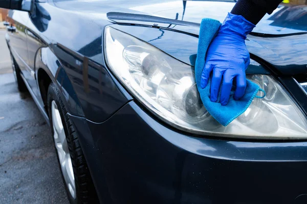 A girl in a blue glove washes the headlight of a car with a blue rag. Car cleaning