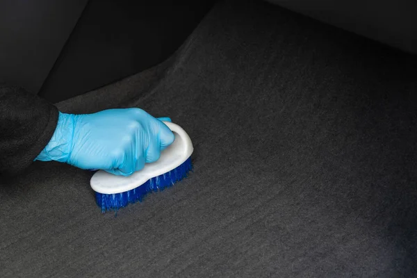 Top view of a hand in a rubber blue glove that is cleaning a gray dirty carpet with a white brush. The concept of cleaning and disinfection of premises. Copy space