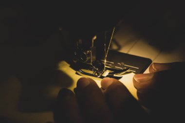 Geceleri dikiş makinesinin üzerindeki kadın eli. Evde para kazanma kavramı. Yakın plan.