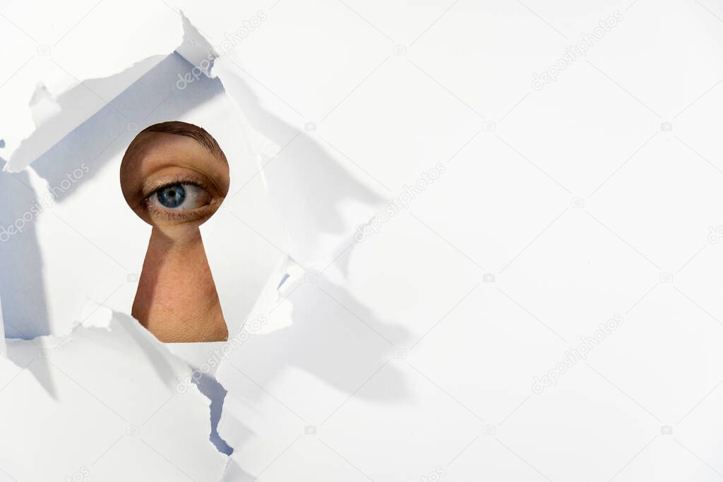 A blue-gray human eye looks through a keyhole-shaped hole. hole in the white paper wall. extreme close-up.