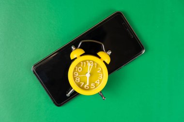 Siyah bir telefondaki sarı çalar saat yeşil bir masanın üzerinde duruyor. Cihazlar üzerinde harcanan zaman. Metin için boş alan