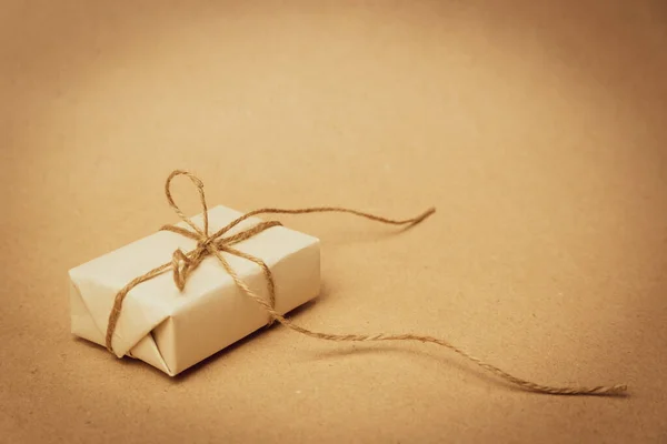 Hediye beyaz kağıda sarılıp bej bir arka planda çuval bezi ipiyle bağlanmış. Retro fotoğrafçılık. Metin girmek için boş alan