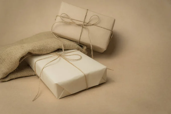 The gift is wrapped in yellowed paper and tied with a burlap rope, in a decorative bag on a beige background. Retro photography. Free space for entering text
