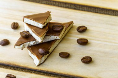 İçi beyaz dolgulu çikolata parçaları birbiri üstüne yığılmış, ahşap arka planda kahve çekirdekleri serpiştirilmiş. Çikolataya kahve döküldü.