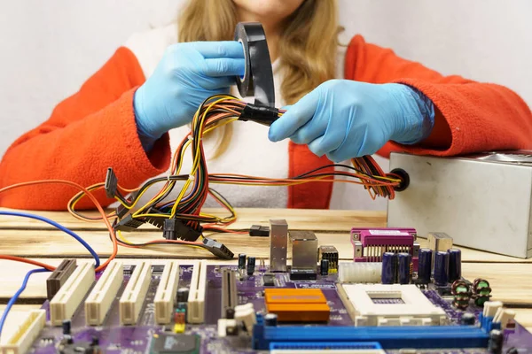 A woman winds electrical tape around the wires. Female hands in rubber gloves wind black electrical tape around colorful wires. Maintenance and repair work in the workshop