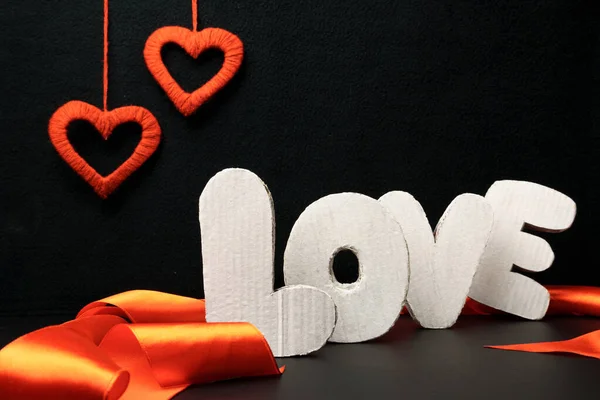 Love made from wooden letters on a black background among red ribbons and hearts. Valentines day decoration