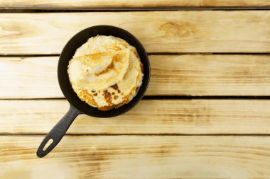 Kırsal siyah bir tavada, ahşap arka planda, fotokopi alanı olan bir yığın ince krep. Yukarıdan görüntüle