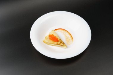 Kırmızı havyarlı bir gözleme siyah arka planda sosla süslenmiş beyaz bir tabakta yatıyor..