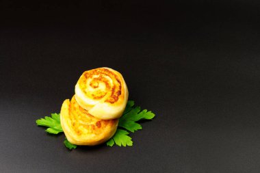 Siyah arka planda maydanoz yapraklarıyla süslenmiş patates rulolarının üst görüntüsü. Kızarmış yemek, atıştırmalık. Hamur içinde patates.