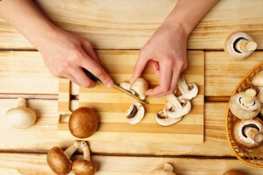 Kesme tahtasında kraliyet mantarlarını dilimleyen kadın elleri. Ahşap arkaplan