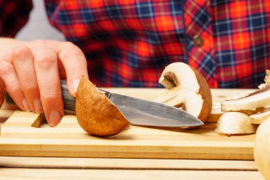 Şefin kareli gömleğinin arka planında bıçak olan dilimlenmiş bir şampiyonun yakın çekimi. Orman mantarı