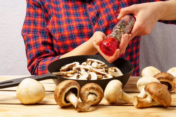 Aşçının dişi elleri tavada mantarlara baharat serpiyor. Yemek pişirmek.