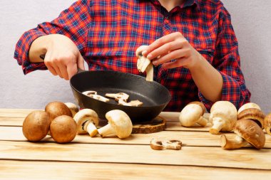 Kız tavaya doğranmış mantar koyar. Kırmızı ekose gömlekli kız ahşap bir masada yemek hazırlıyor.
