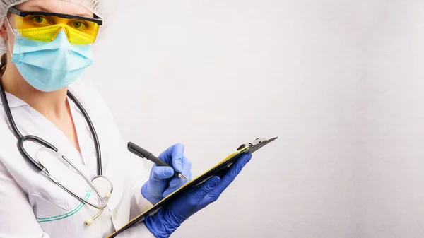 A doctor in a protective suit fills out a registration form during the coronavirus pandemic. Gray background with copy space