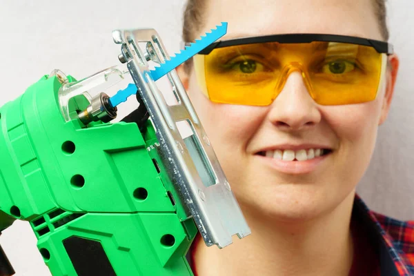portrait of a worker with a jigsaw. close-up of a woman in safety glasses holding an electric jigsaw.