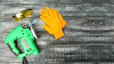 Kişisel koruyucu ekipmanlar ve elektrikli aletler. Elektrikli yapboz, güvenlik gözlükleri ve eldivenler siyah tahta masada fotokopi alanı ile.