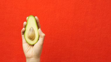 Avokado elinde. Kırmızı arka planda olgun avokado tutan bir kadın. Sağlıklı yaşam tarzı