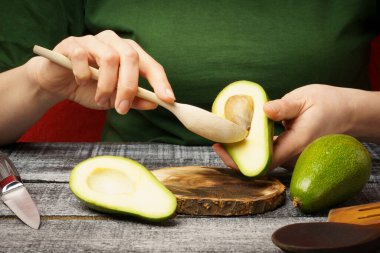 Kız ahşap bir kaşıkla avokadoyu temizliyor. Masada taze avokadosu olan genç bir kadın var.