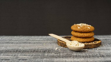 Bir yığın yulaf ezmeli kurabiye ve siyah beyaz ahşap arka planda rulo yulaflı ahşap kaşık.