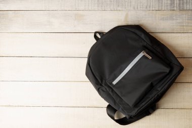 Metin için kopyalama alanı olan beyaz ahşap arkaplan üzerine siyah sırt çantası