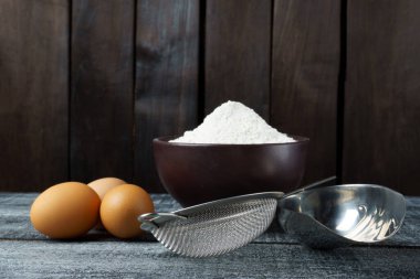 Koyu arkaplanda makarna yapmak için malzemeler. Mutfak masasında un ve yumurta var..