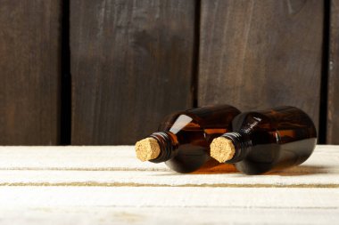 Mantar tıpalı kozmetik cam şişe. Kahverengi şişeler beyaz masada, siyah ahşap duvara karşı.