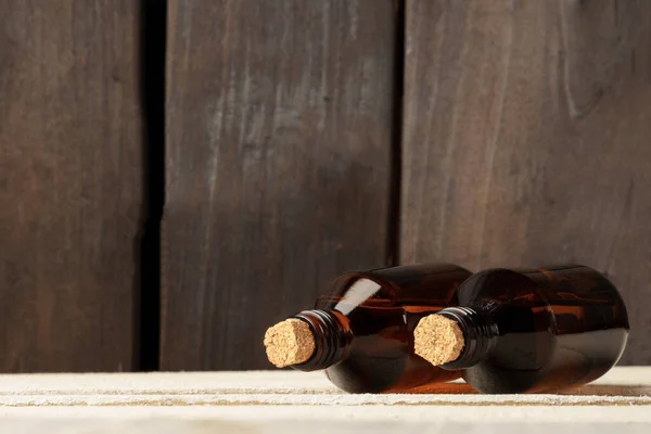 cosmetic glass bottle with cork stopper. brown bottles on white table against dark wood wall