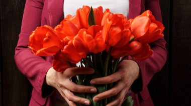 Koyu ahşap arka planda, kadın ellerinde kırmızı lale demeti.