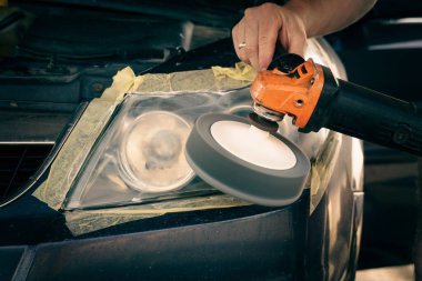 Tampon bir makineyle farları temizliyorum. Usta arabanın farlarını parlatır..