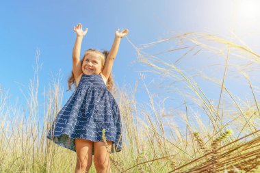 Mavi elbiseli küçük neşeli kız, mavi güneşli gökyüzüne karşı, tutamaklarını gökyüzüne doğru çekiyor. Pankart