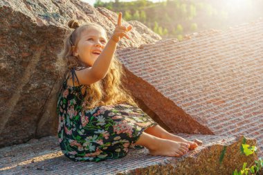 Taşların üzerindeki küçük neşeli kız parmağını gökyüzüne doğrultuyor, güneş onu aydınlatıyor. Pankart