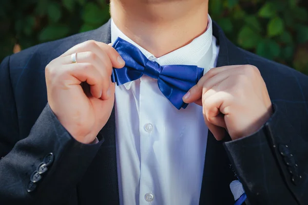 The groom adjusts his bow tie hands in the park — Stock Photo, Image