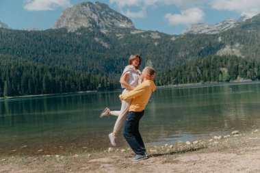 Güzel bir dağ ve gölün kıyısında kucaklaşan çift. Nazikçe sarılıp birbirine aşık çiftin güzel bir doğa geçmişine sahip öpücüğü. Kayalık dağların önünde göl.