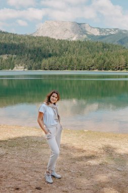 Karadağ Durmitor Milli Parkı 'ndaki göl, orman ve dağlara bakan bir kız. Turist kız gölün, kozalaklı ormanın ve dağlardaki turkuaz gölün kıyısındaki büyük taşın üzerindeki sihirli manzaranın tadını çıkarıyor. Yürüyüş.